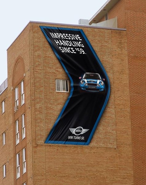 Реклама автомобиля BMW MINI на стене жилого дома демонстрирует его маневренность на городских дорогах.